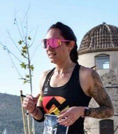 Irene, corredora, avanzando con esfuerzo y concentración durante una carrera al aire libre, mostrando su determinación en cada paso.