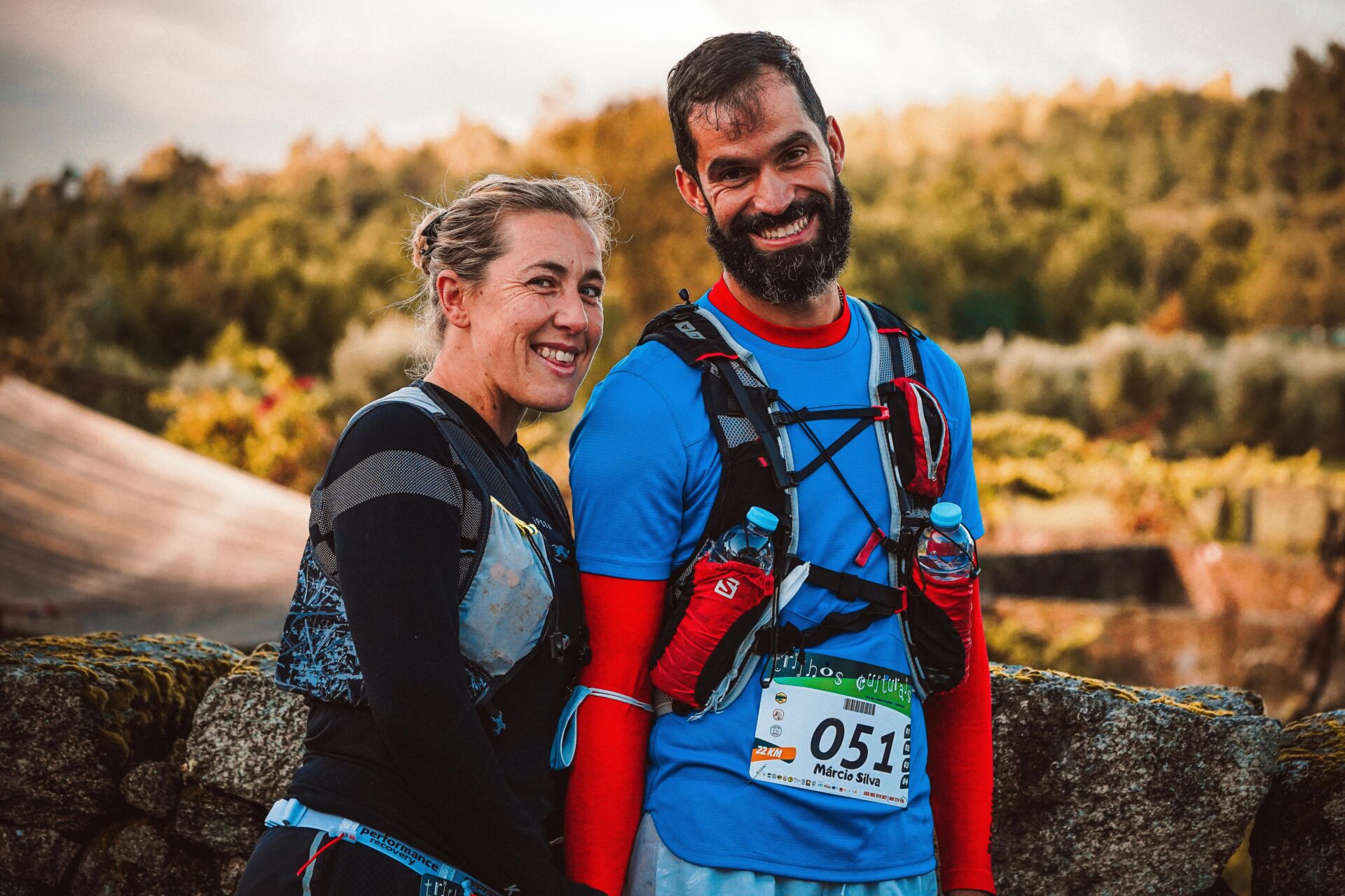 Pareja de trail runners corriendo juntos por un sendero montañoso, disfrutando de la naturaleza y avanzando con determinación durante una carrera de trail.